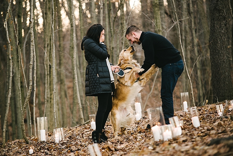 man in black sweater smiling at golden retriever while woman in black coat stands nearby