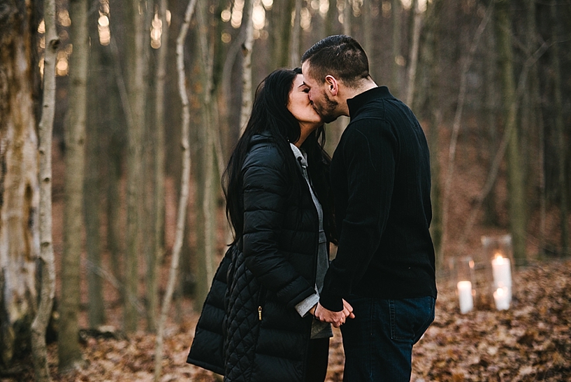 couple kissing in woods in winter with candles around