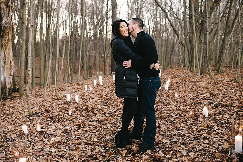 woman laughing while man in black sweater kisses her cheek in woods