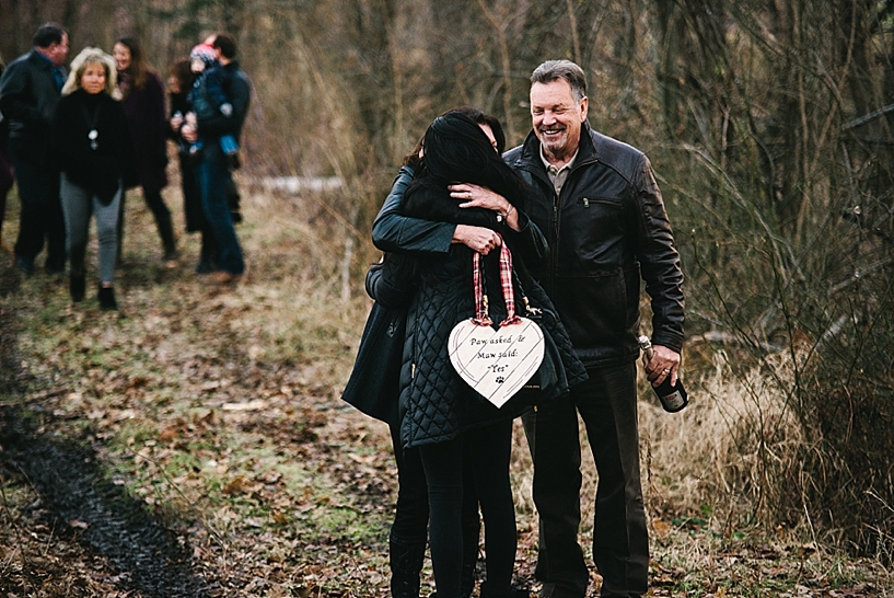 newly engaged woman hugs her parents in woods