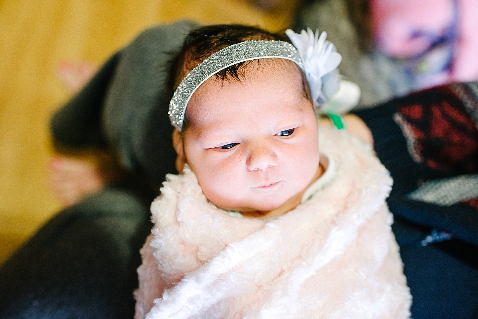 newborn baby girl wrapped in pink fuzzy blanket with glittery headband on and dark hair
