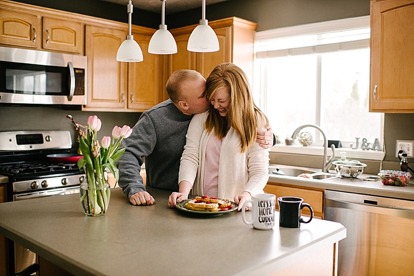 husband hugs wife and kisses her cheek standing at kitchen island