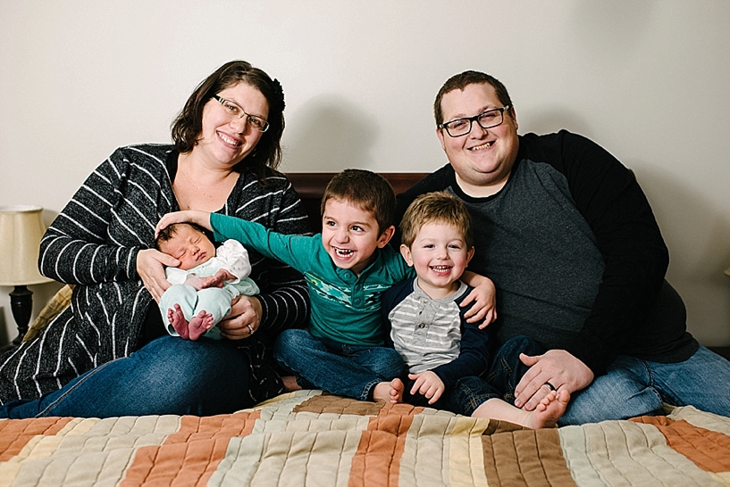 family sitting on bed laughing with two boys and newborn daughter