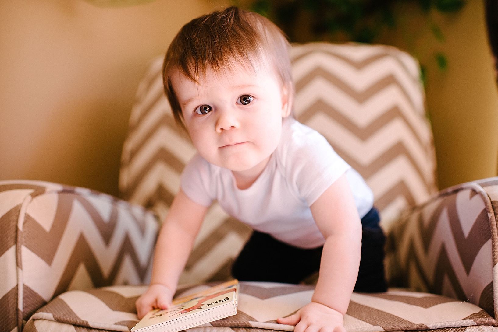 toddler boy in white onesie sitting on chevron chair with serious look on face