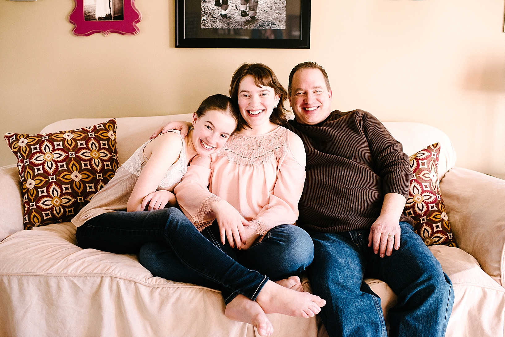 father and two teenage daughters sitting on couch smiling