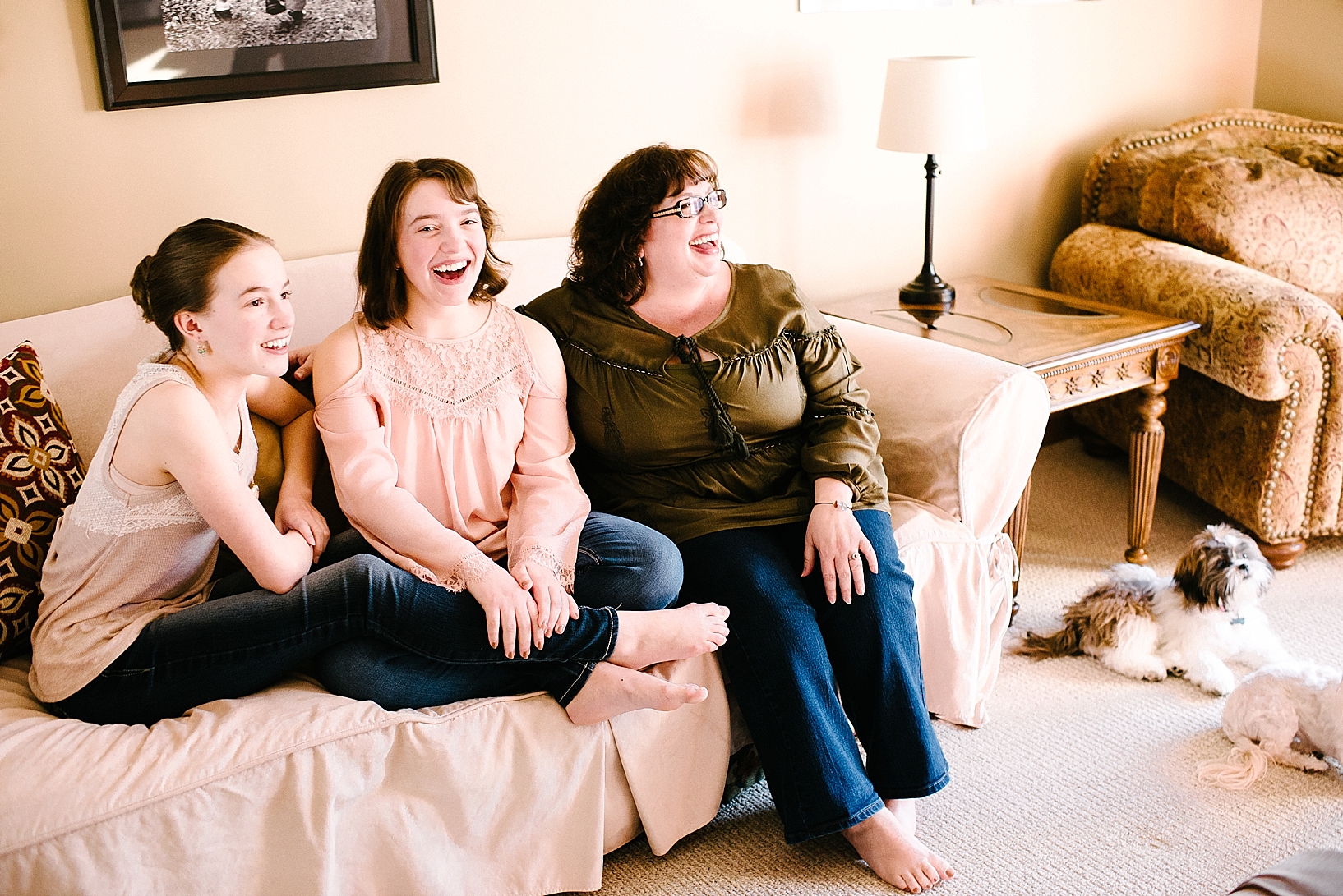mom and two teenage daughters sit on couch in living room laughing