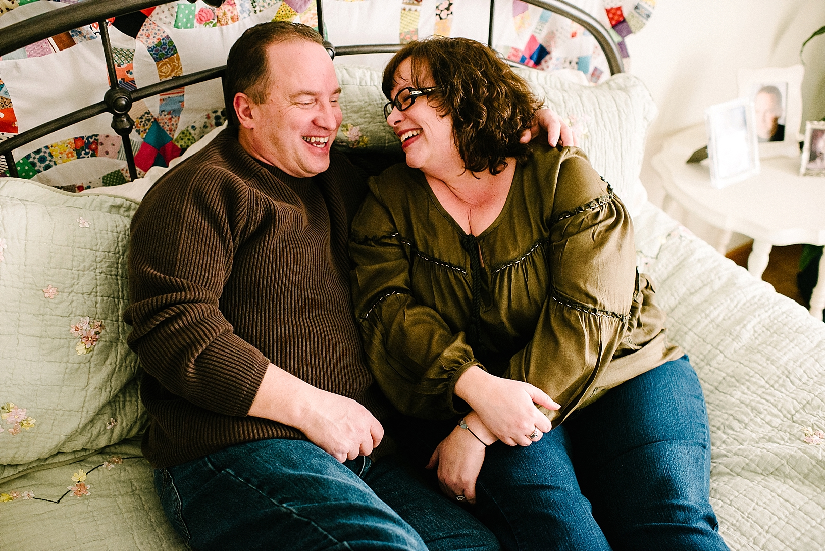 husband and wife lay on their wrought iron bed laughing during home session