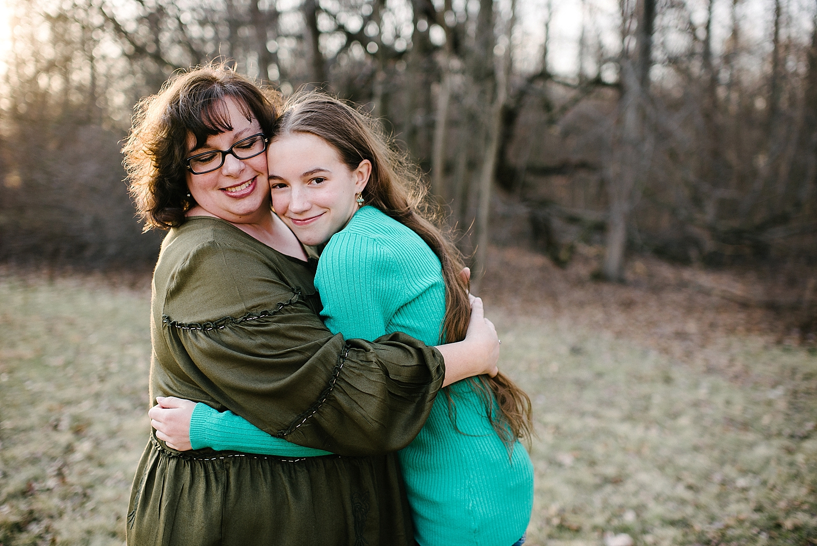 woman with short curly hair and glasses wearing green shirt hugging teen daughter with long brown hair