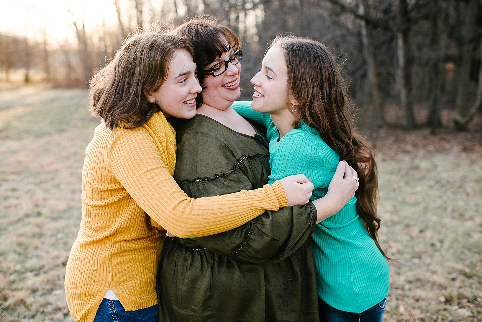 mother hugging two teenage daughters in backyard