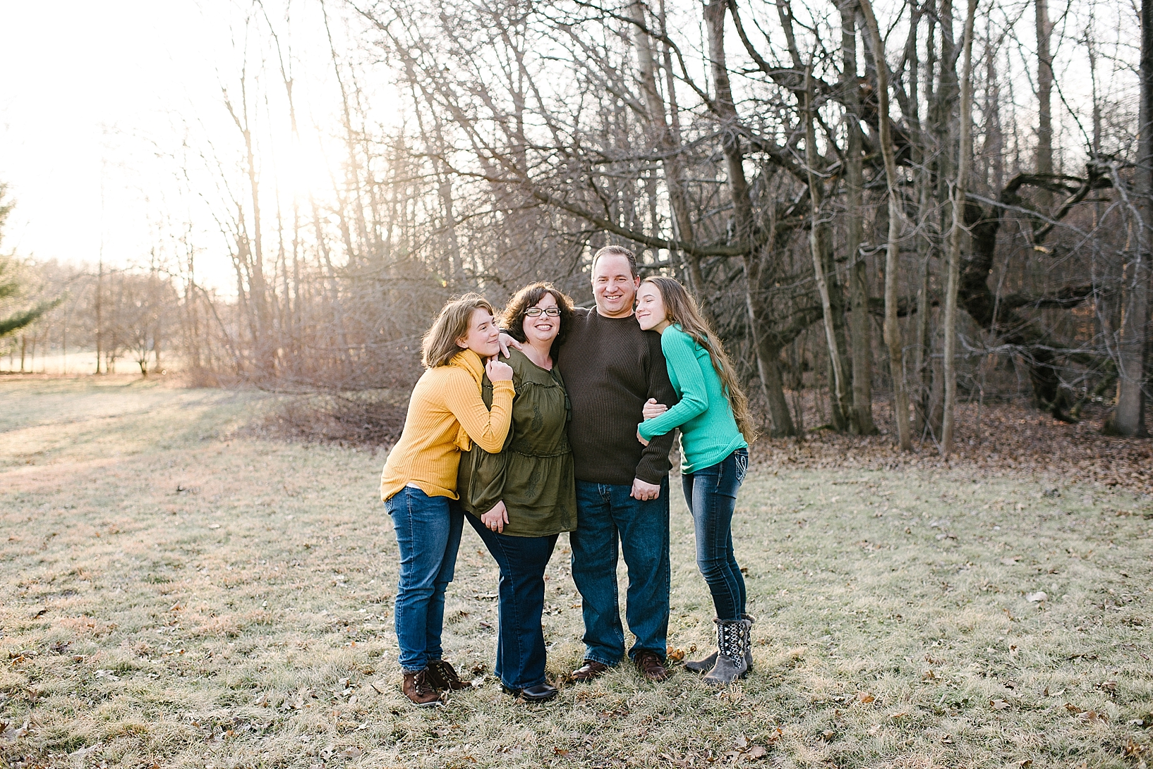 family with two teen daughters standing in their backyard with woods surrounding