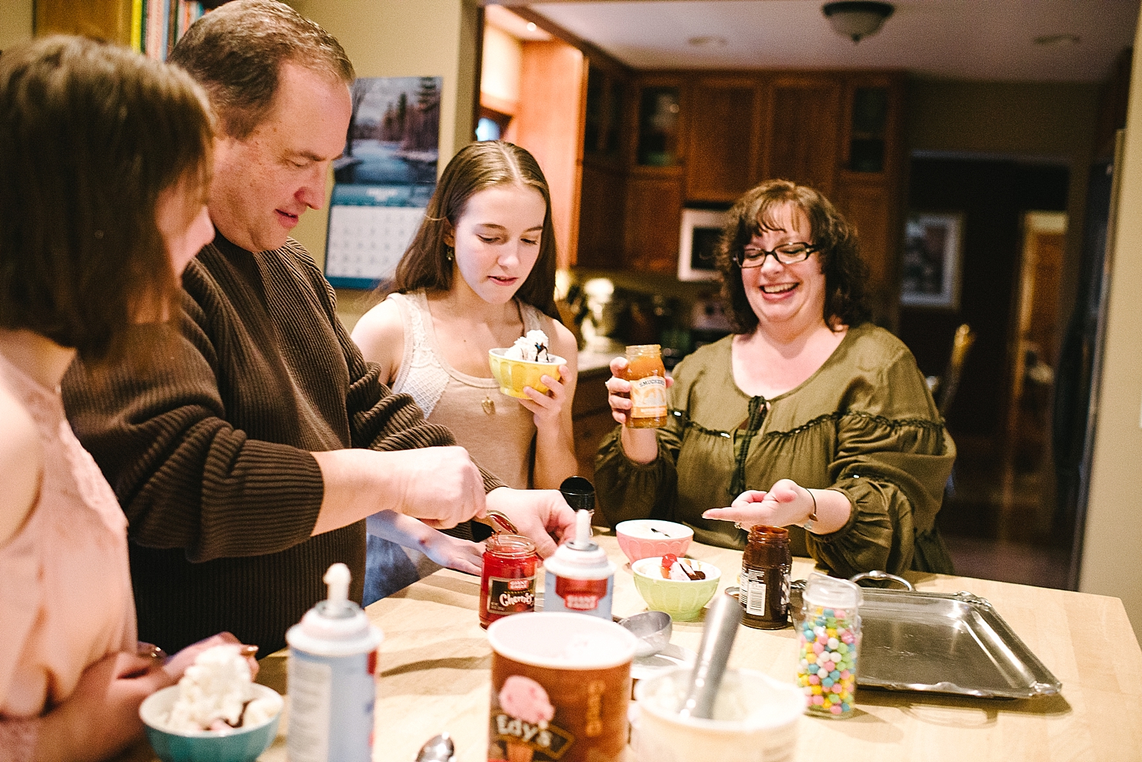 family making ice cream sundaes in kitchen