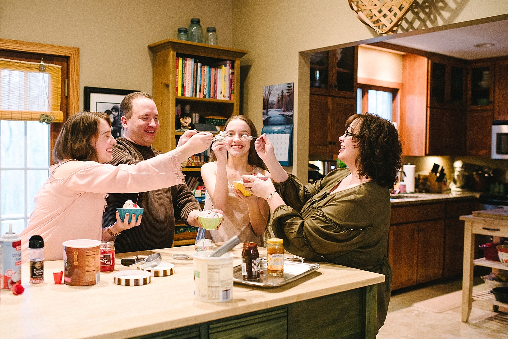 family clinking spoons together while eating ice cream sundaes in kitchen