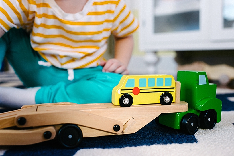 little boy in teal pants and yellow striped shirt playing with trucks