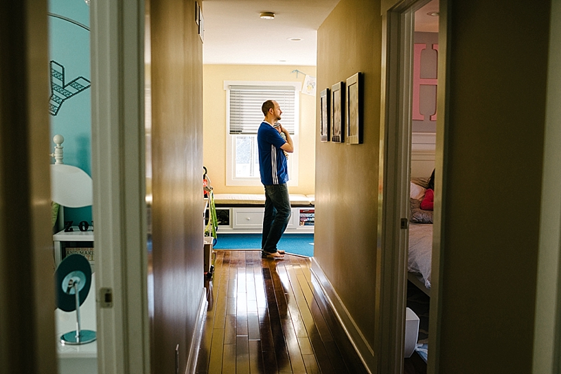 father holding newborn baby walking down hallway of house