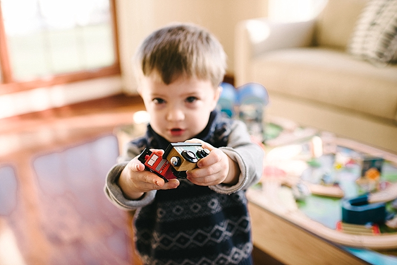 toddler boy wearing sweater holding trains in his hands