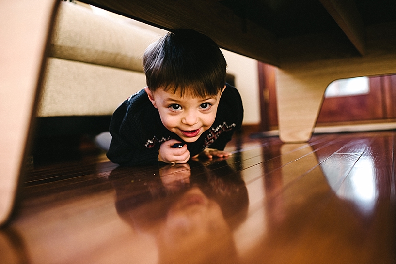 toddler boy laying on wooden floor peeking under coffee table