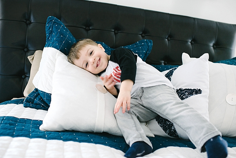 toddler boy laying on bed with blue and white sheets