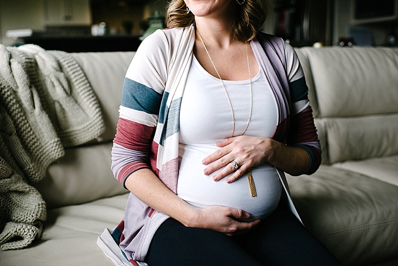 pregnant woman sitting on living room couch wearing striped cardigan and long necklace