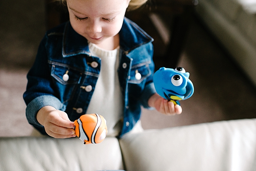 little girl wearing denim jacket holding dory and Nemo toys in hand