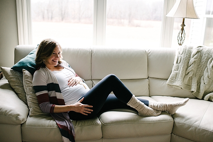 pregnant woman wearing striped cardigan and cozy socks laying on couch smiling
