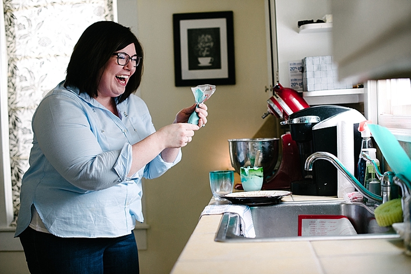 woman with dark hair and glasses making icing in kitchen laughing