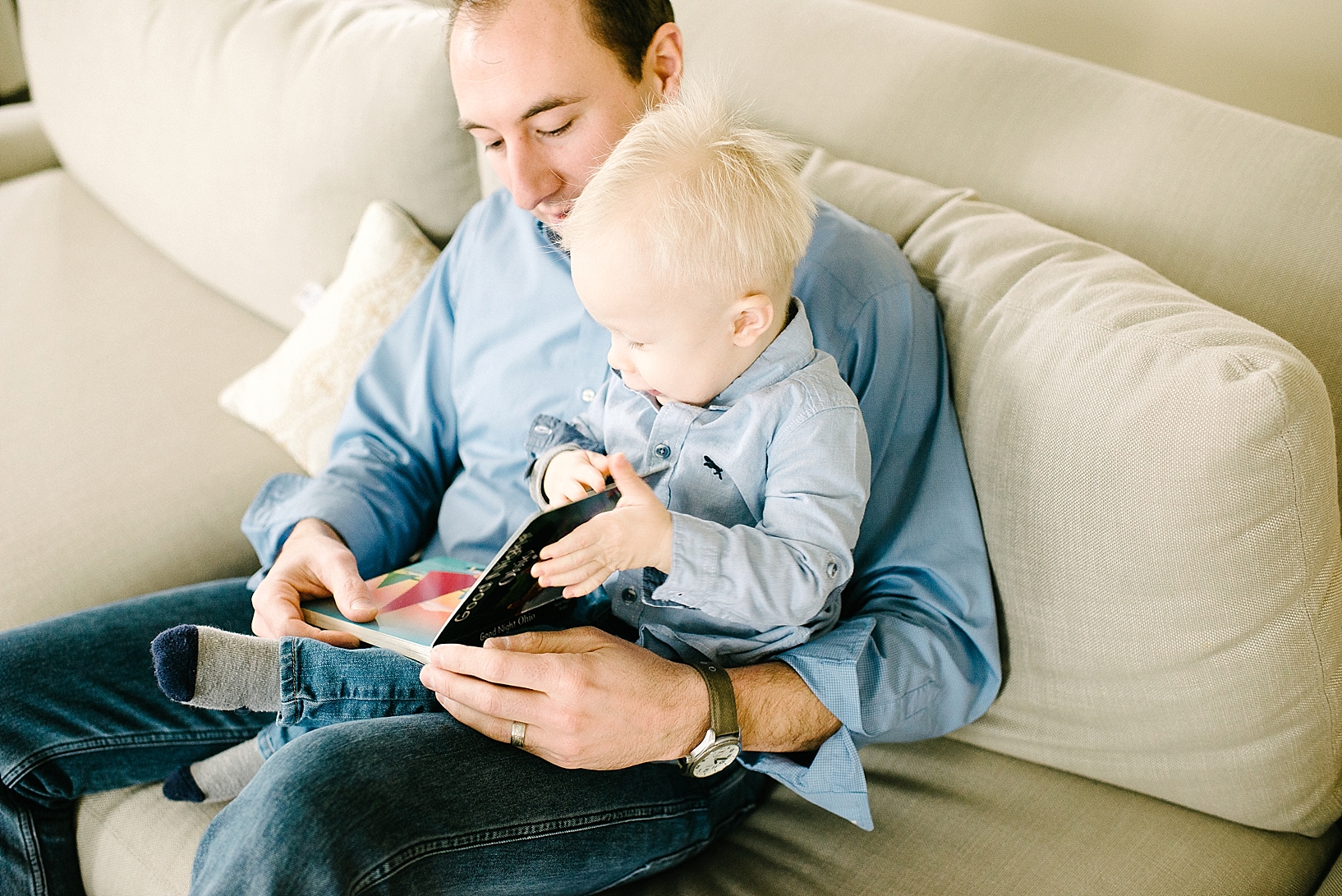 dad sitting on couch reading books with toddler son on his lap