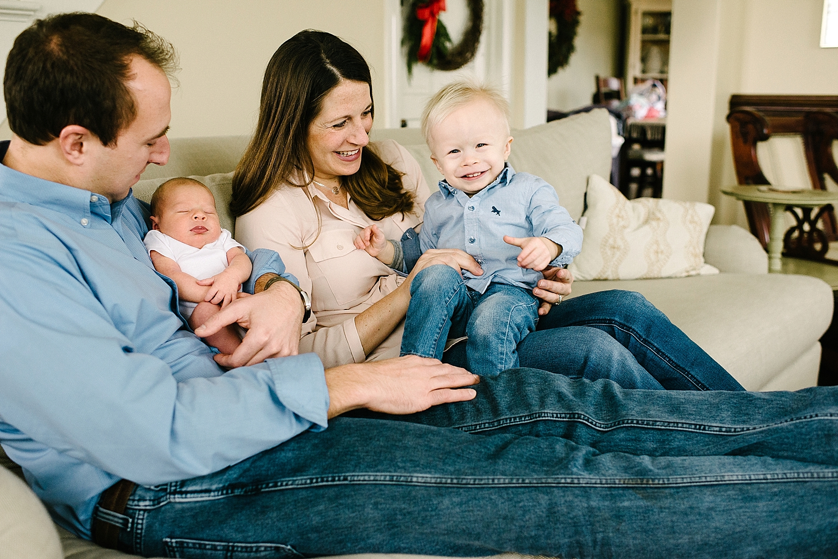 man and woman sitting on couch with toddler boy and newborn baby girl in their arms smiling