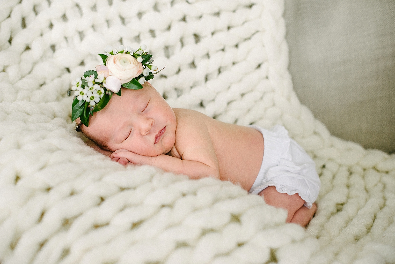 newborn baby girl wearing white bloomers and floral crown laying on cream knit blanket