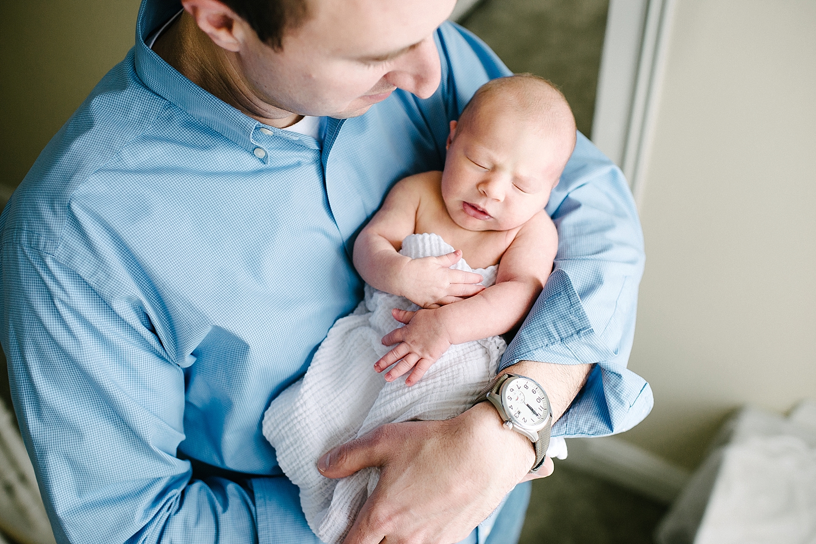 man in blue dress shirt holding newborn daughter in his arms