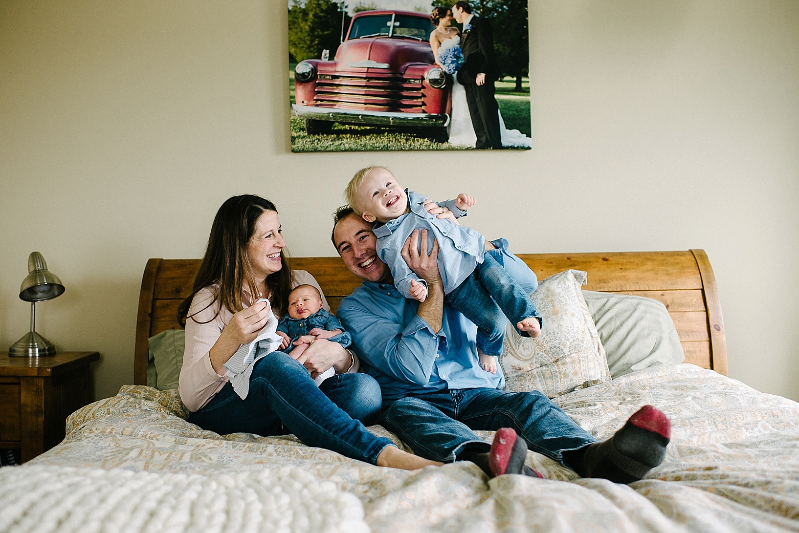 parents with toddler son and newborn daughter sitting on bed laughing