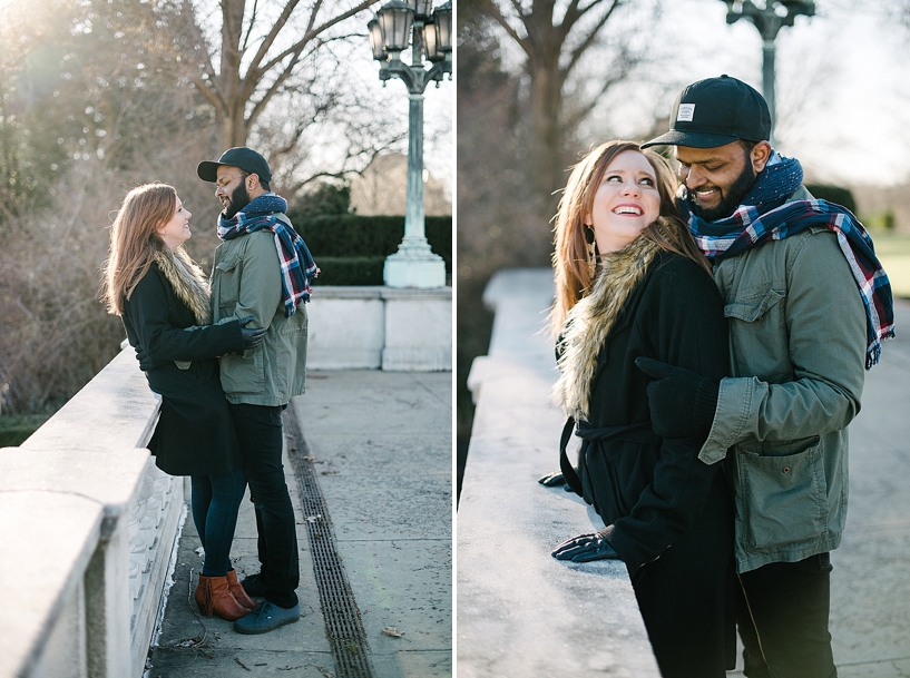 Indian man in green coat and scarves hugging redhead woman in black coat with fur collar
