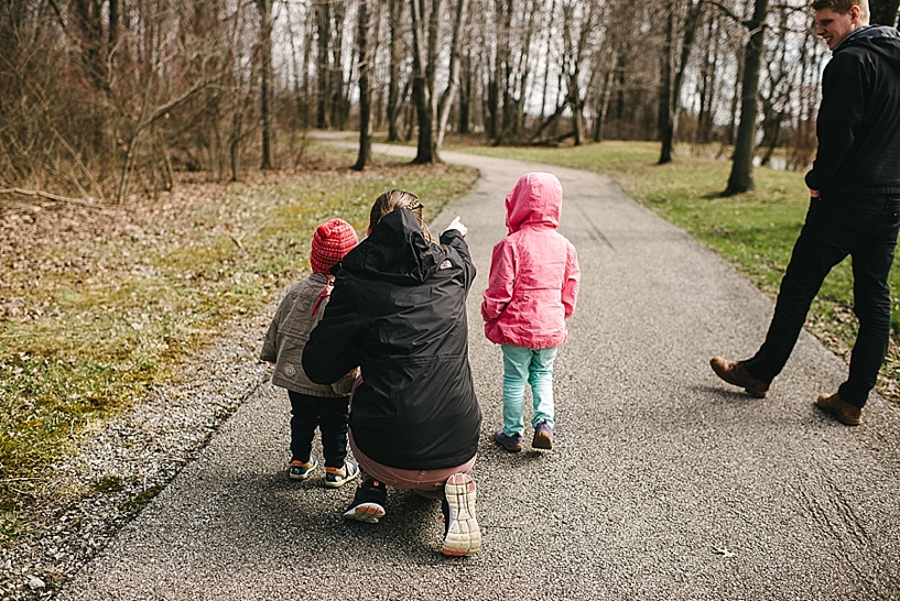 mother kneeling next to son and daughter on walking path pointing into woods