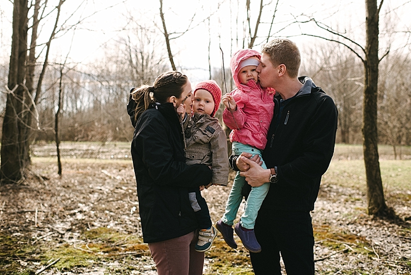 mom and dad holding young son and daughter kissing them on cheeks