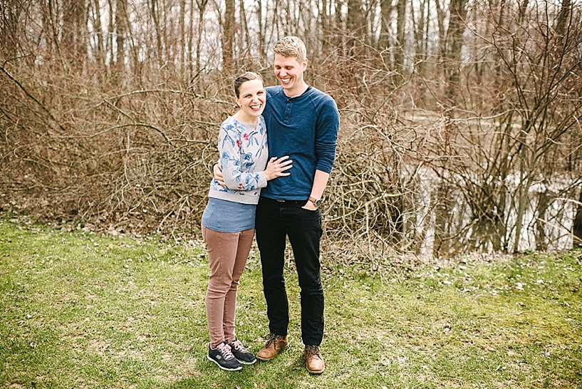 couple standing in woods with arms around each other laughing