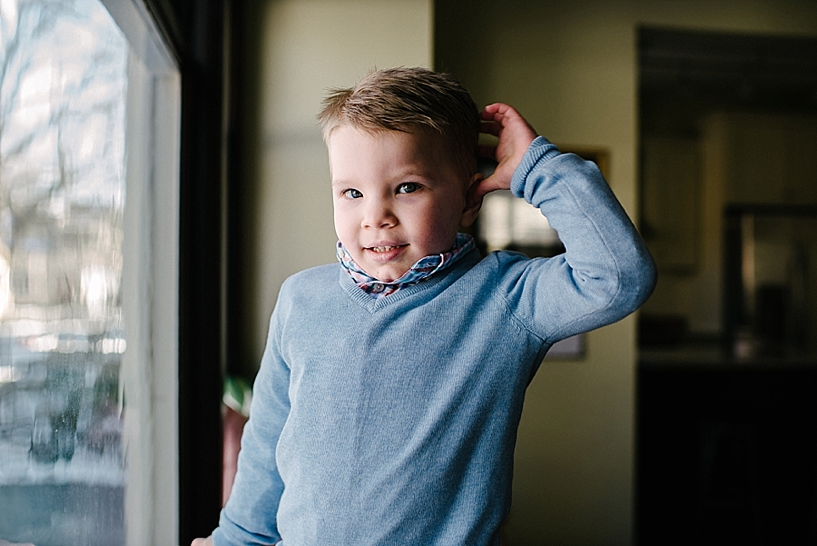 two year old boy wearing blue sweater standing by window in dining room