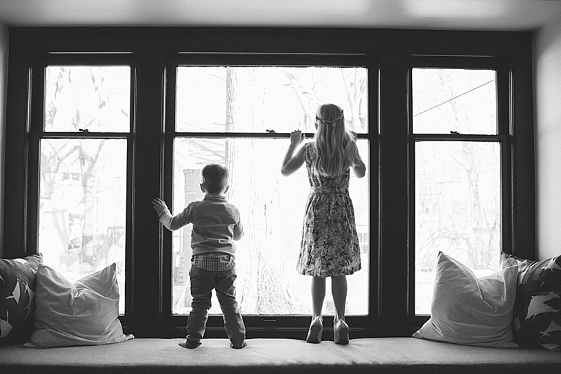 silhouette of boy and girl standing in front of big picture window in home
