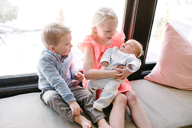 young boy and girl sitting on window seat holding their newborn baby brother