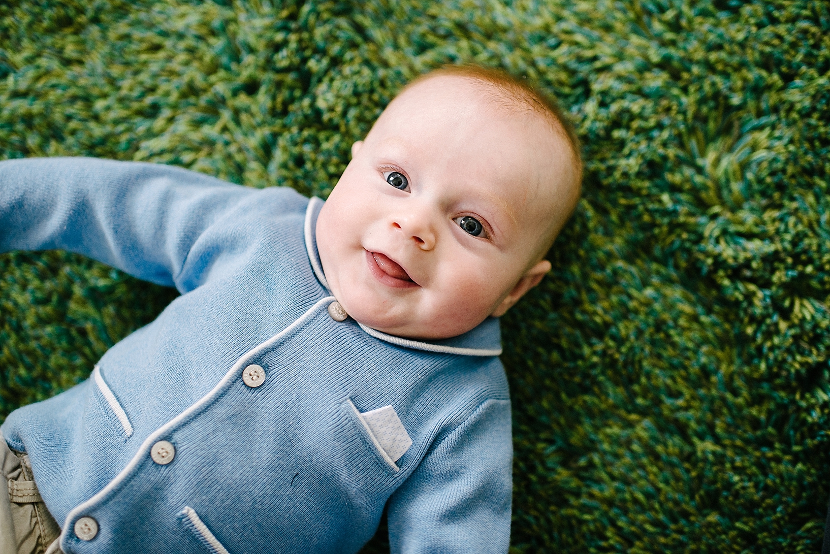 redhead infant wearing blue cardigan laying on green carpet