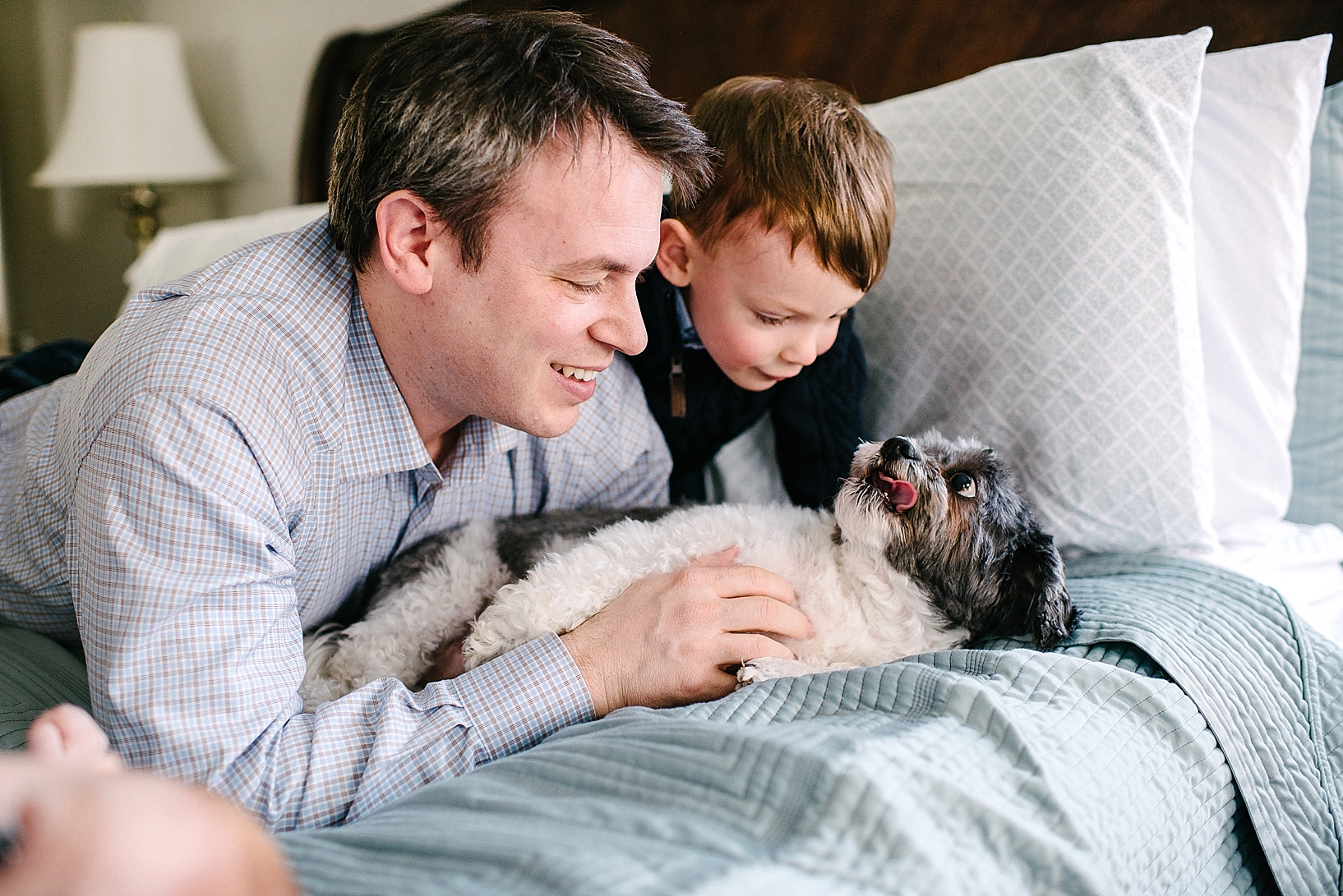 dad and son laying on bed petting dog