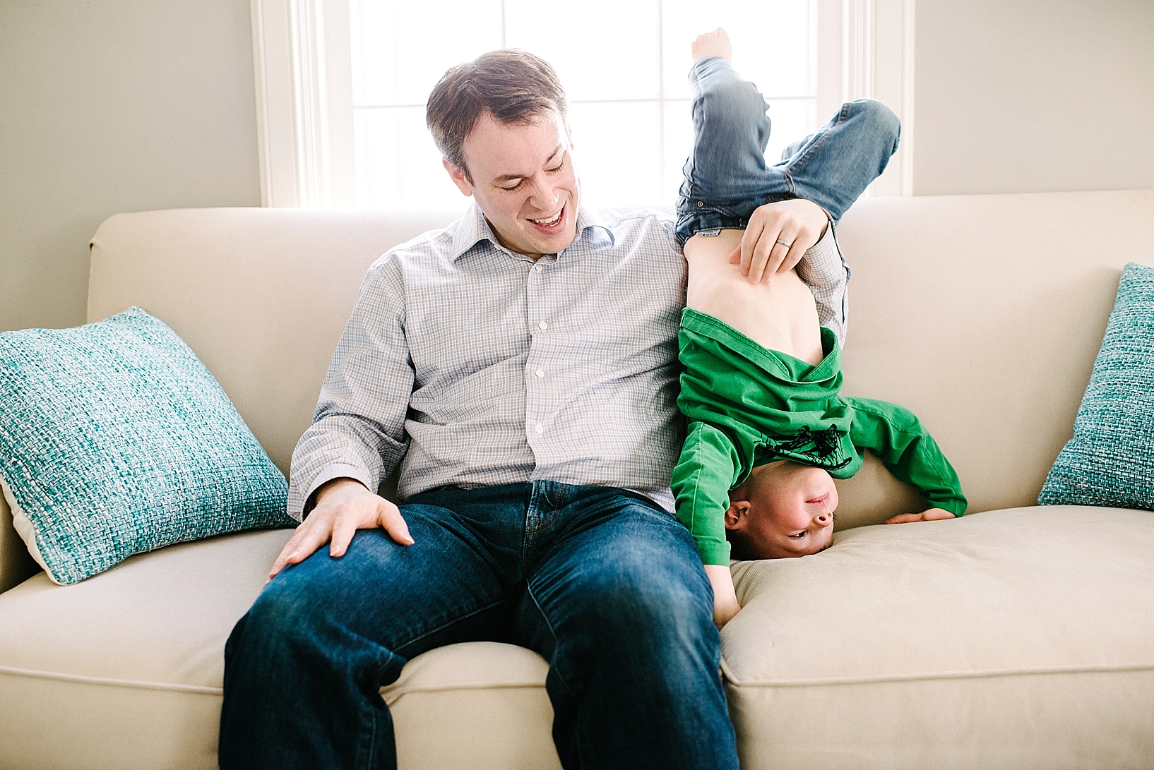 dad sitting on couch with son upside down next to him