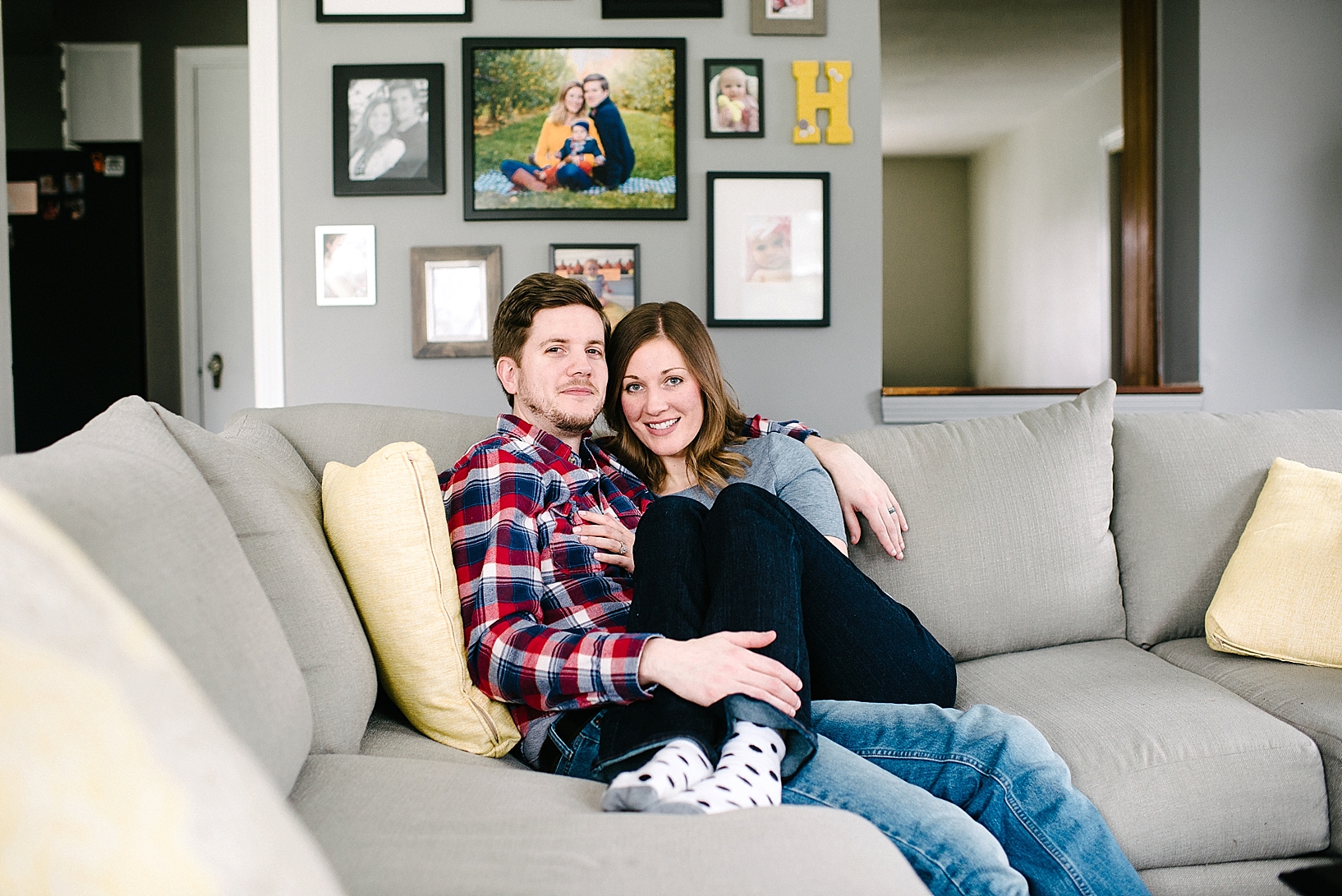 couple sitting on grey couch with yellow pillows in front of photo wall