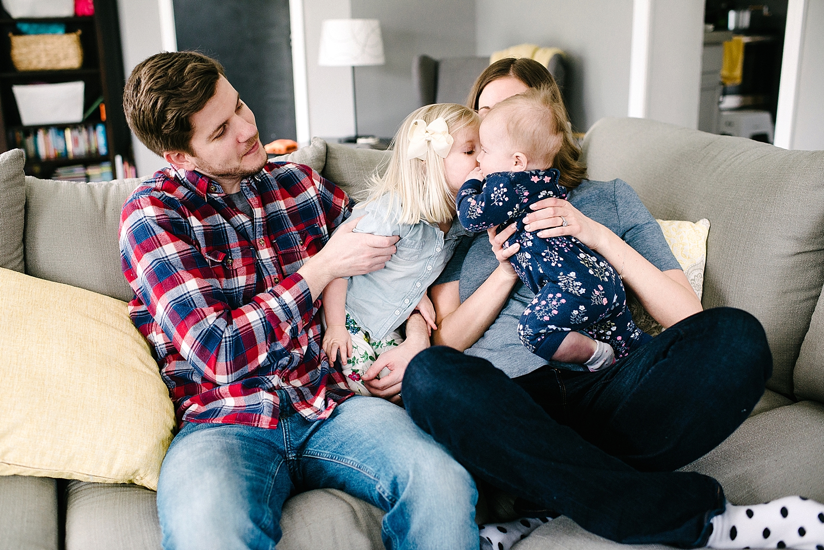 parents sitting on couch holding young daughters giving each other a kiss