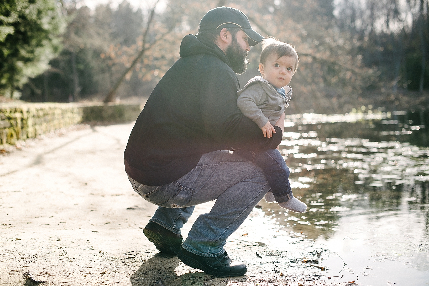 man kneeling by pond holding son on his knee