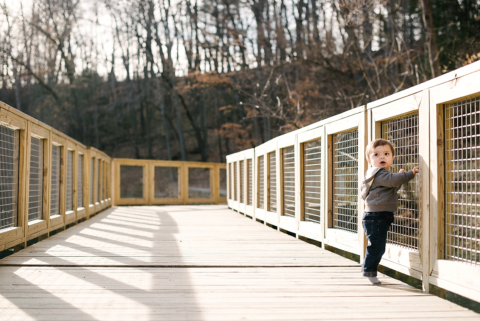 little boy standing on bridge holding onto rail