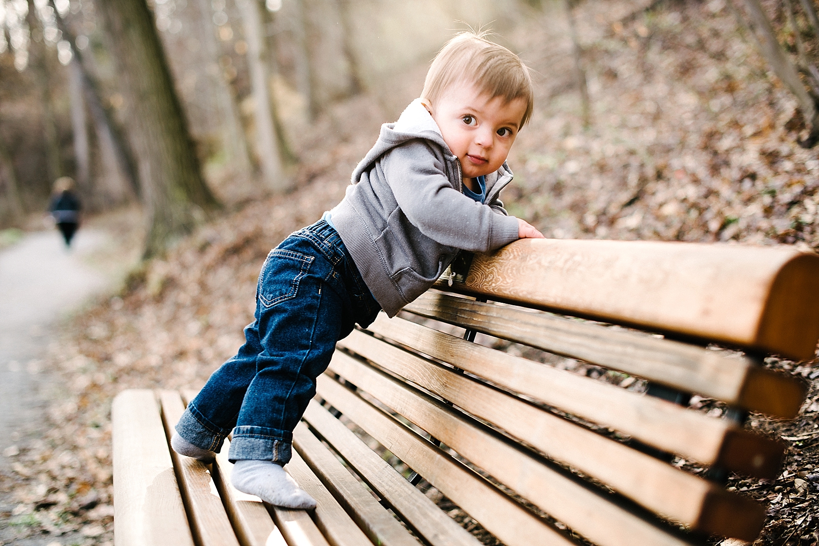 one year old boy wearing jeans and grey hoodie standing on park bench