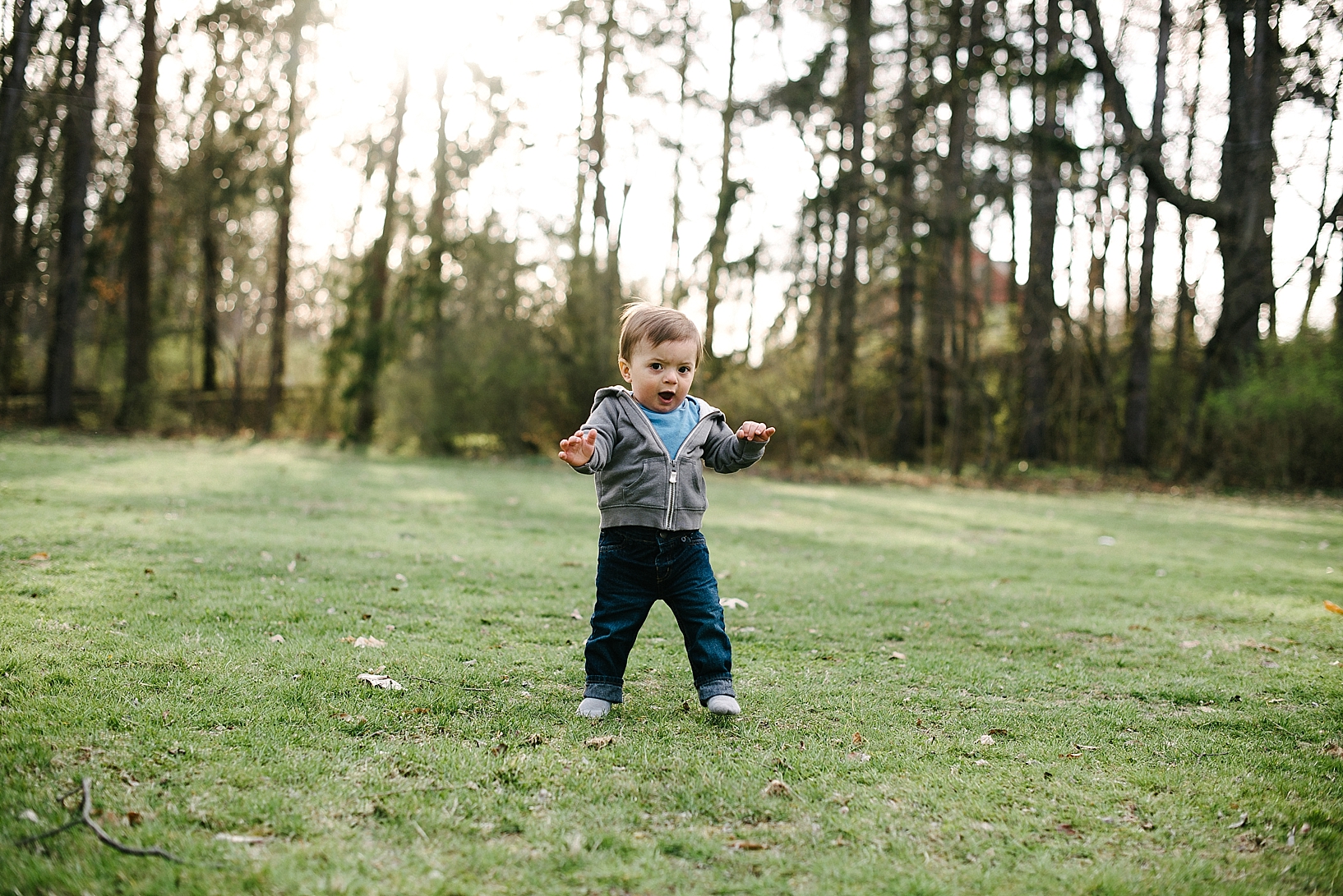 one year old boy wearing grey hoodie and jeans walking down grassy hill
