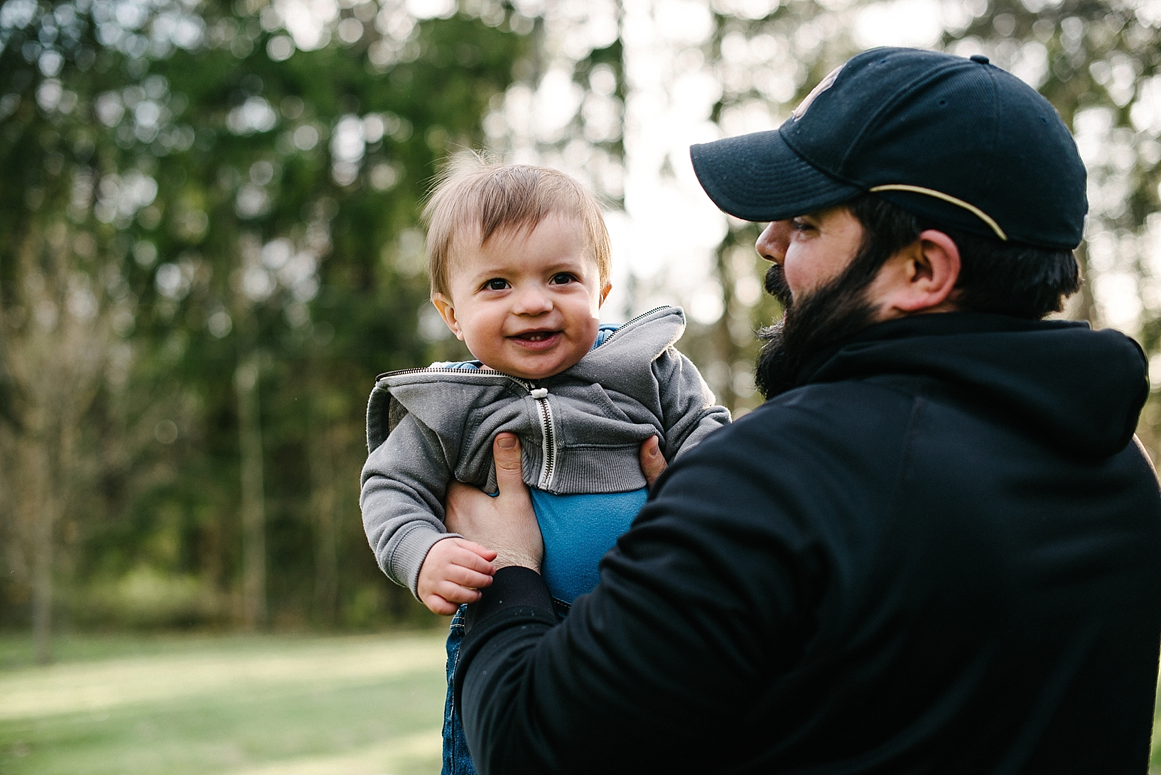 dad with beard wearing baseball hat holding son and smiling