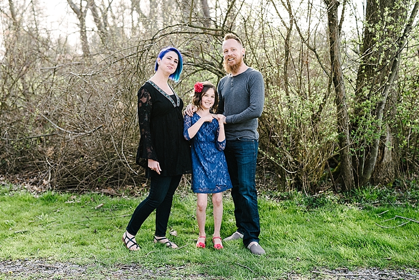 woman with blue hair and man with red beard standing with daughter in wooded area
