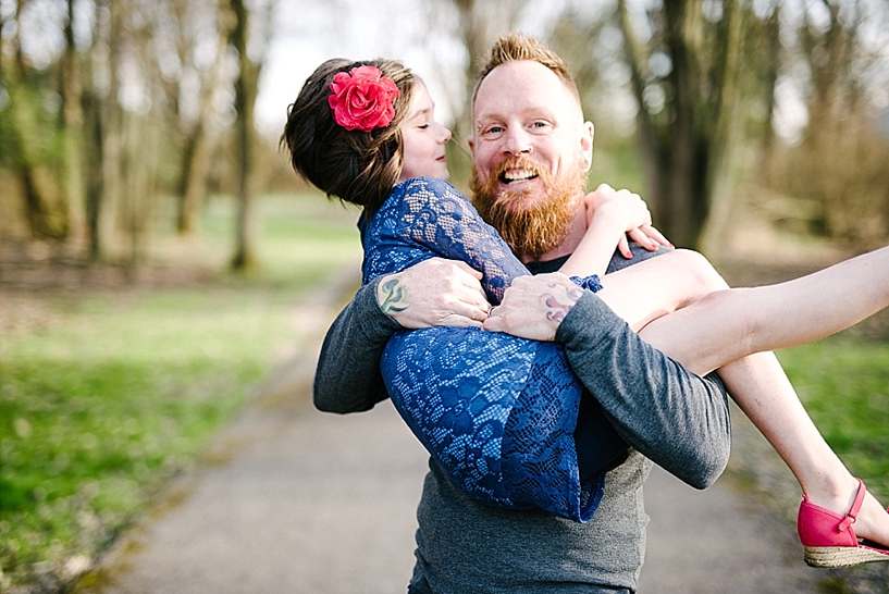 dad with beard and tattoos holding young daughter wearing blue lace dress in his arms