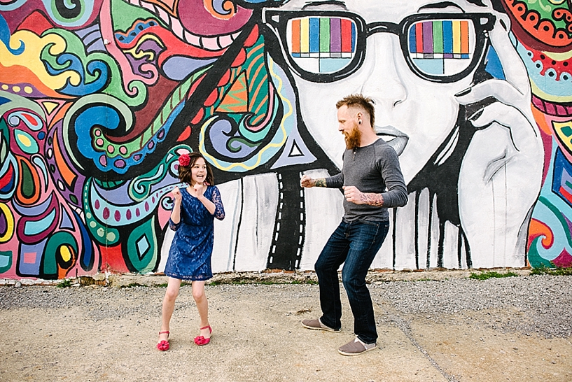 dad and daughter dancing in front of colorful graffiti mural